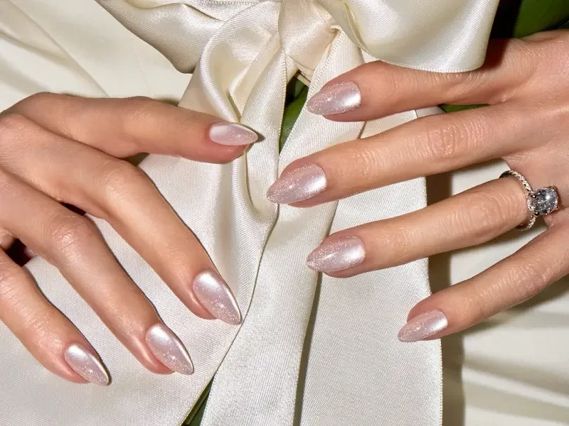 A hand with pearly almond press-on nails resting on ivory silk