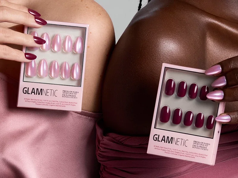 Two hands holding Glamnetic press-on nail boxes in pink and burgundy sets