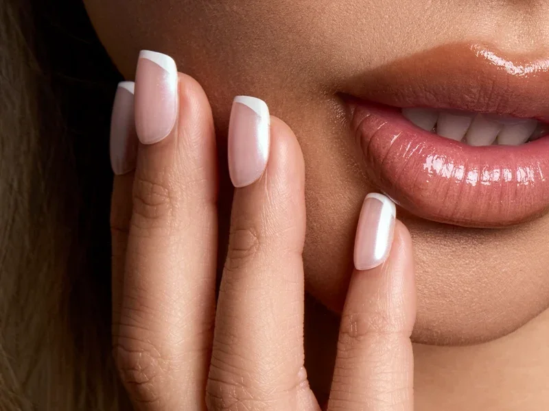 Close-up of a hand with white French tip press-on nails resting by the lips